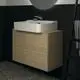 Waschtisch mit rechteckigem Becken in Weiß, kombiniert mit einem hellen WTU-Schrank aus Eiche. Ideal Standard Spiegel darüber, Armatur am Becken installiert. Schwarz geflieste Wand.